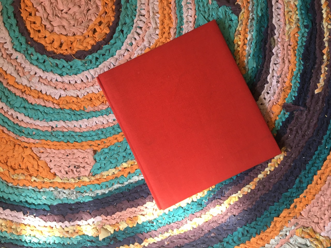 A red photo album on my colorful concentric circle rag rug in my apartment in Boston.