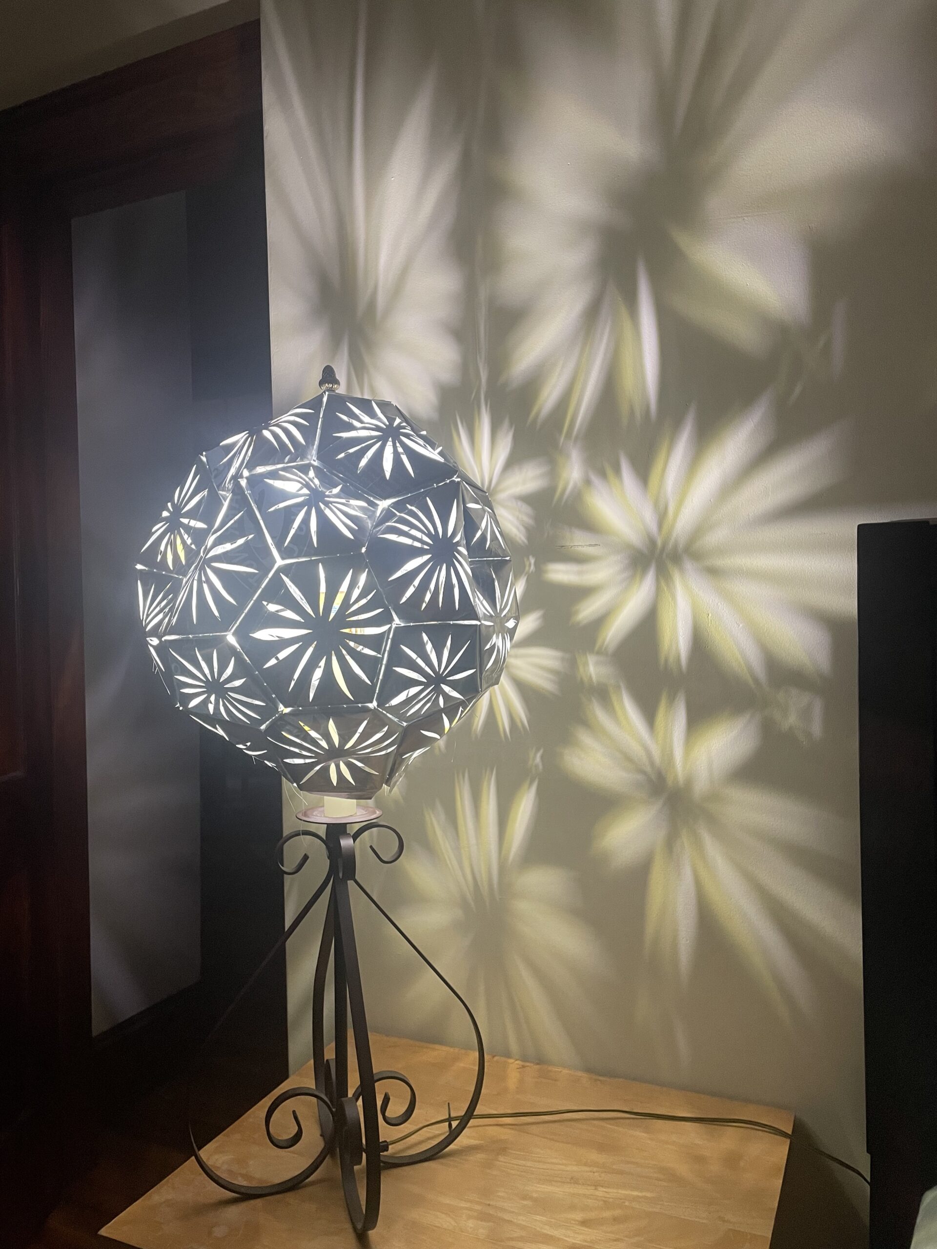 A silver light with cut outs casts shadows on the wall resembling a dandelion.